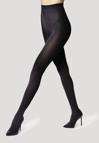 Collant neri opachi con una vita alta, texture liscia e design aderente, abbinati a scarpe nere con tacco alto.