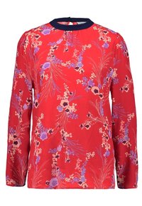 Rote Bluse mit langen Ärmeln und hohem Kragen mit marineblauem Besatz, filigranen Blumenmustern in Lila, Pink und Weiß sowie glattem Stoff.