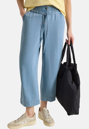 Persona che indossa pantaloni cropped a gamba larga azzurri con vita elastica e tiene una borsa tote nera trapuntata.
