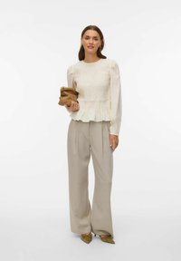 Krēmkrāsas blūze ar pūstā tipa piedurknēm un vairākkārtēju volānu apakšu, kopā ar gaiši pelēniem plaša piegriezuma biksēm un olīvu zaļas nedaudz smailas formas kurpēm. Rokās turot brūnu somiņu.