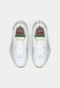 Witte sportieve sneakers met een bovenwerk van mesh en leer, gouden accenten en een dikke rubberen zool. Beschikken over veters en een logo aan de zijkant.