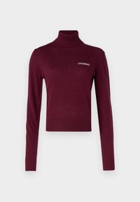 Bordo turtlenecko stilius megztinis, priglustantis, ilgomis rankovėmis ir raukšlėmis ant rankovių. Ant krūtinės yra mažas logotipas. Minkšta mezginio tekstūra.