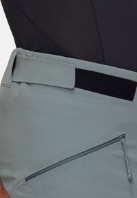 Ceinture gris clair avec une fermeture à crochet et boucle, dotée d'une poche zippée sur le côté et d'une finition lisse et texturée.