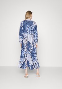 Lange, vloeiende jurk met een patchworkontwerp in blauwtinten met bloemmotieven, lange mouwen en een losse pasvorm die onder de knie valt.