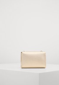 Clutch dorato con texture, di forma rettangolare, chiusura a zip e una leggera lucentezza, posato su una superficie grigia chiara su uno sfondo uniforme.