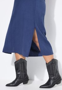 Marineblauwe textuurjurk met een zijsplit, gecombineerd met zwarte cowboylaarzen versierd met zilveren studs en een puntige neus.