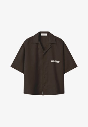 Chemise noire à manches courtes boutonnée avec col et texte blanc "another" sur la partie gauche de la poitrine.