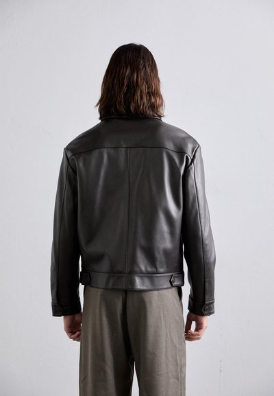 Black leather jacket with a structured design, flat collar, and adjustable side tabs. Smooth texture with subtle stitching details.