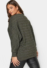 Lös passform, texturerad topp i mörkgrön och grå ränder. Har avsmalnande ärmar och rund halsringning. Kombinerad med svarta byxor.