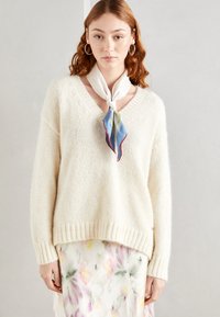 Suéter de punto color crema con escote en V, dobladillo acanalado y mangas largas, combinado con una falda de estampado floral y una bufanda de seda ligera.