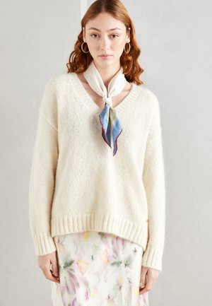 Suéter de punto color crema con escote en V, dobladillo acanalado y mangas largas, combinado con una falda de estampado floral y una bufanda de seda ligera.