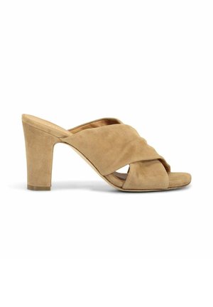 Mule en daim beige à talon haut avec larges brides croisées et bout carré ouvert sur fond blanc.