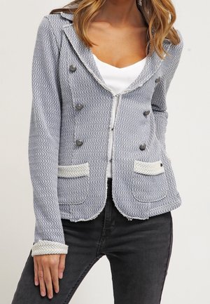 Chaqueta texturizada en gris y blanco con botones de doble pecho, dos bolsillos frontales y un dobladillo ligeramente deshilachado. Corte ajustado con cuello.