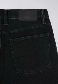 Jeans in denim nero con una tasca posteriore e una semplice etichetta in pelle in vita. Il tessuto ha una consistenza liscia con dettagli di cucitura sottili.