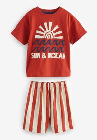 T-shirt en coton rouge avec un motif de soleil et de vagues, associé à un short crème à rayures verticales rouges ; taille élastique pour le confort.