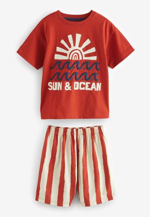 Punane puuvillane T-särk, millel on päikese ja laine graafika, koos kreemja lühikeste pükstega, millel on punased vertikaalsed triibud; elastne vöökoht mugavuse tagamiseks.