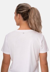 Camiseta de algodón blanca con mangas cortas, que presenta un cuello redondo y un pequeño detalle del logo en la parte superior de la espalda. Textura suave.