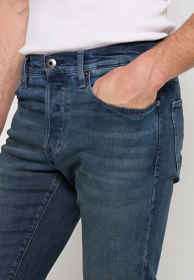 Jeans en denim bleu foncé avec une coupe slim, dotés d'une taille standard, de poches avant et d'un léger délavage pour un look épuré.