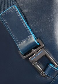 Correa de cuero azul marino con hebilla metálica, presenta costuras y detalles en azul, mostrando una textura suave y un diseño moderno.