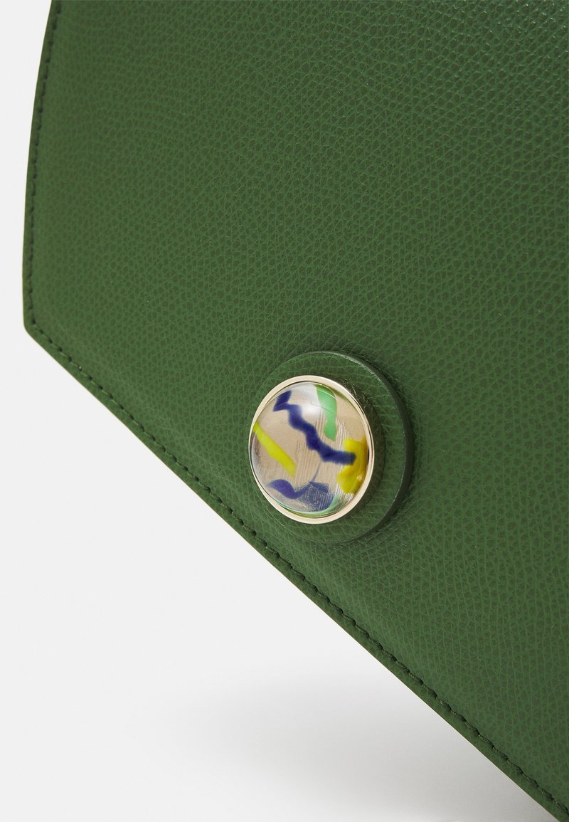 Roh zelené texturované kožené tašky s kulatým, multibarevným tlačítkem s průhlednou kopulí a okrajem ve zlatém odstínu.