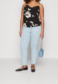 Camicetta nera floreale con fiori bianchi, jeans skinny azzurri, e ballerine nere. Piccola borsa azzurra con tracolla a catena.