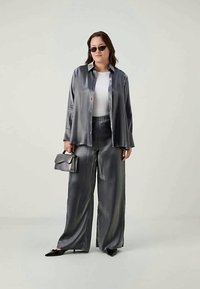 Blusa de seda cinza e calças de perna larga, combinadas com óculos de sol pretos e uma pequena mala de ombro. Textura suave com um acabamento brilhante.