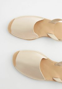 Sandali in pelle beige con punta aperta, dettagli cuciti e un design a cinturino. Texture liscia e forma minimalista.