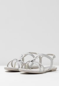 Hopeat sandaalit, joissa on ristikkäinen hihnapaino, tasapohja ja säädettävä nilkkahihna, valmistettu tukevasta materiaalista pitävän otteen varmistamiseksi.