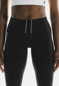 Leggings neri a vita alta con una texture liscia, dotati di chiusura con cordino e di un piccolo logo sul lato sinistro.
