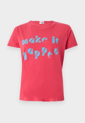 Henkilö, jolla on päällään punainen t-paita, jossa on teksti "make it happen", valkoiset housut, mustat balleriinat ja joka pitää kädessään mustaa kudottua käsilaukkua valkoisella taustalla.