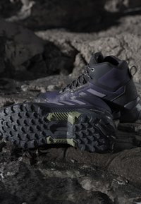 Dark hiking boots with rugged soles resting on rocky, uneven terrain, highlighting grip and durability for outdoor use.