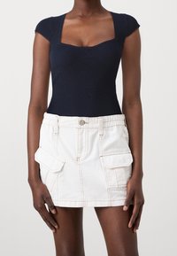 Marinblå ribbad bodysuit med fyrkantig halsringning kombinerad med en vit denimminikjol med sidofickor och kontrasterande sömmar.