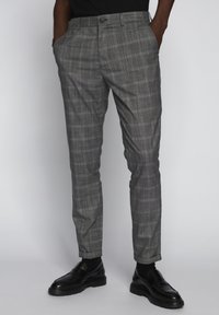 Šedé kostkované kalhoty z lehké látky, rovného střihu, s bočními kapsami a knoflíkovým zapínáním v pase, v kombinaci s černými botami.