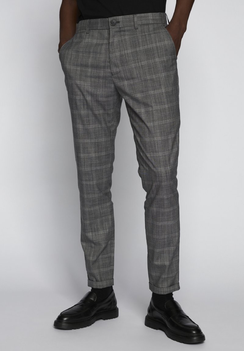 Šedé kostkované kalhoty z lehké látky, rovného střihu, s bočními kapsami a knoflíkovým zapínáním v pase, v kombinaci s černými botami.
