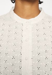 Weiße bestickte Bluse mit rundem Kragen, durchgehender Knopfleiste und zarten Blumenmustern im gesamten Stoff.