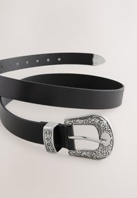 Cintura in pelle nera con fibbia decorativa in argento caratterizzata da un intricato motivo floreale. Design semplice con molteplici fori per la regolazione.