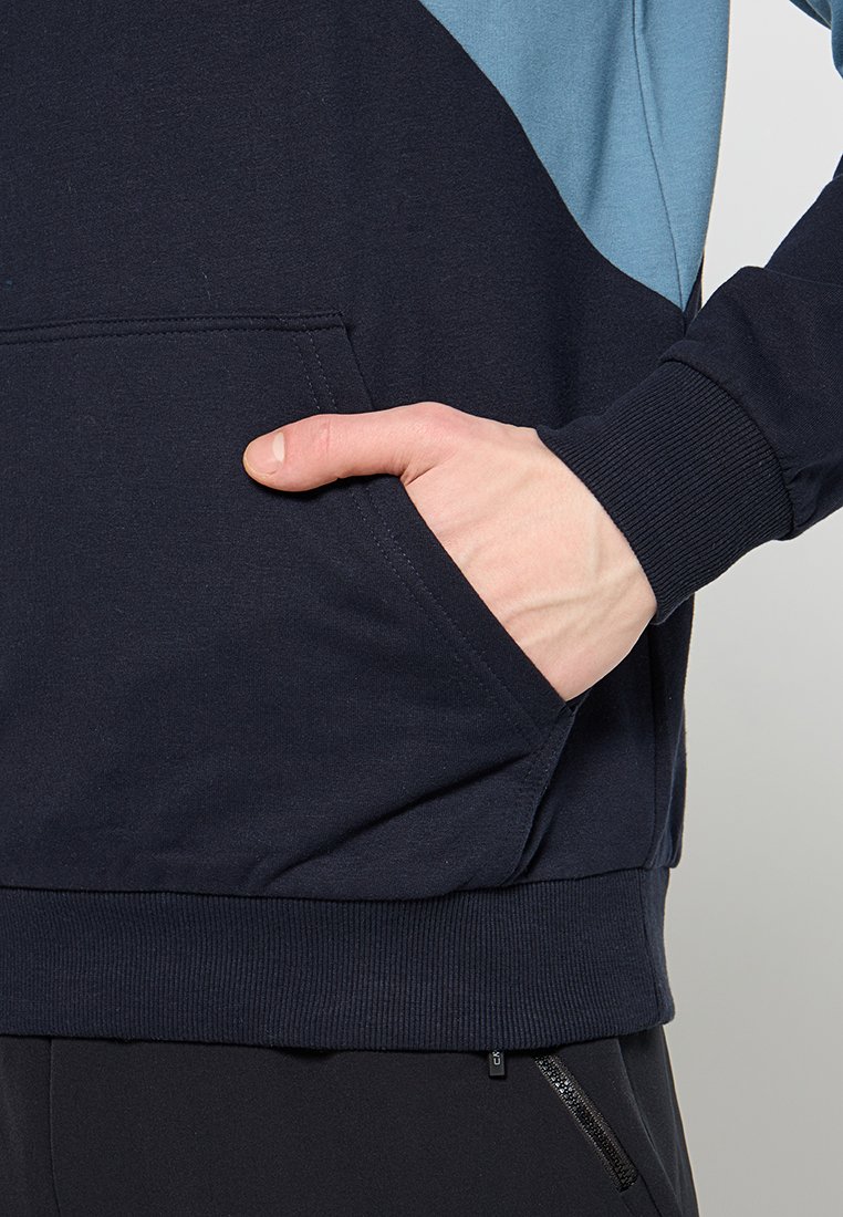 Felpa con cappuccio blu navy e azzurro chiaro, in misto cotone, presenta una tasca a marsupio, polsini a coste e orlo texturizzato. Dettaglio con zip sul lato.