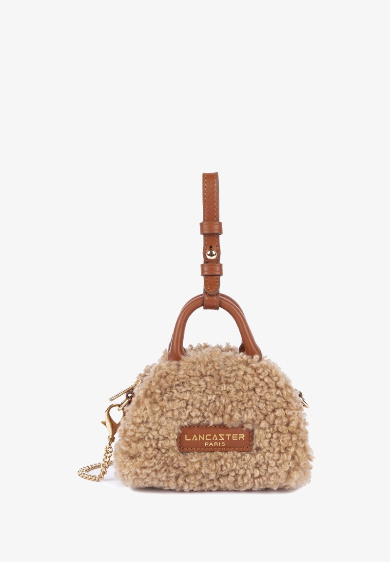Borsa di colore tan con una texture morbida, accenti in pelle marrone, manico corto e hardware dorato. Presenta il logo su una patch in pelle.