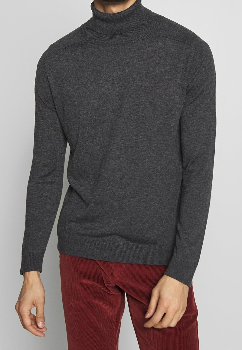 Dunkelgrauer Rollkragenpullover aus einem weichen Stoff, mit langen Ärmeln, geripptem Kragen und Saum sowie klassischer Passform. Kordhose sichtbar.