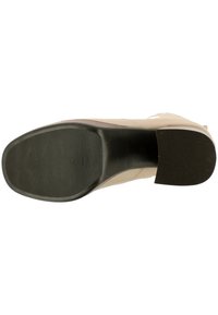 Beige hooggehakte schoen met een glad bovenwerk, ronde neus en een zwart rubberen zool met structuur. Hak heeft een lichte helling.