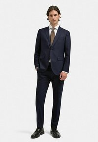 Mörkblå kostym med slim fit, enfärgad kavaj, flikiga slag och matchande byxor, kompletterad med en ljus skjorta och randigt slips.