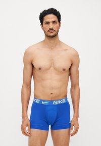 Modri bokserice iz gladkega materiala s potiskanim belim elastičnim pasom z logotipom "NIKE". Tesno prilegajoča zasnova.