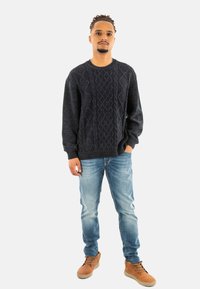Pullover in maglia blu scuro con un motivo a diamante testurizzato, abbinato a jeans in denim blu chiaro e scarpe stringate color tan.