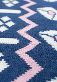 Tessuto tessuto blu con un motivo geometrico e accenti bianchi e rosa, tra cui forme a zigzag e diamante. La texture appare morbida.