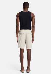 Zwarte mouwloze tanktop en beige shorts met elastische taille en twee achterzakken. Gladde stof, standaard pasvorm en knielange ontwerp.