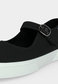 Μαύρο παπούτσι στιλ Mary Jane με ρυθμιζόμενο λουράκι και ασημένια αγκράφα, με παχύ λευκό υφασμάτινο καουτσούκ σόλα.