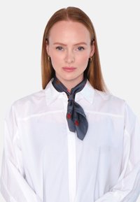 Grå silkesjal bundet rundt halsen, med et rødt geometrisk mønster, båret over en hvit skjorte med krage. Glatt tekstur og klassisk design.