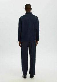 Mornarsko modra strukturirana jakna s kratkim ovratnikom in dolgimi rokavi, v kombinaciji s prugastimi hlačami v ujemajoči barvi. Gladka tekstura.