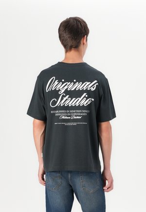 Black cotton t-shirt with a loose fit, featuring white "Originals Studio" lettering on the back and a round neckline.