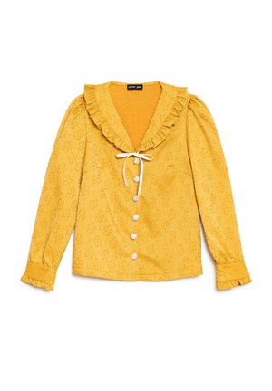 Blouse jaune à manches longues avec texture florale, col et poignets à volants, boutons en perles blanches et un lien blanc au niveau de l'encolure.